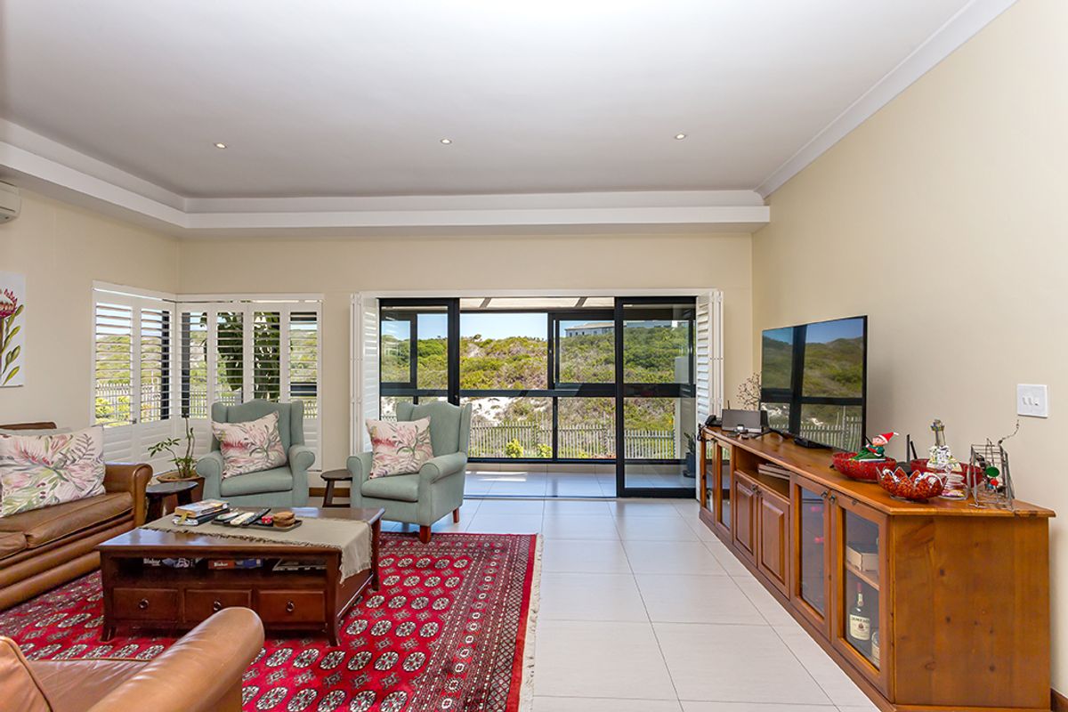Spacious living room featuring tiled floors, recessed ceiling detail, and large sliding glass doors opening to an outdoor area with plantation shutters.