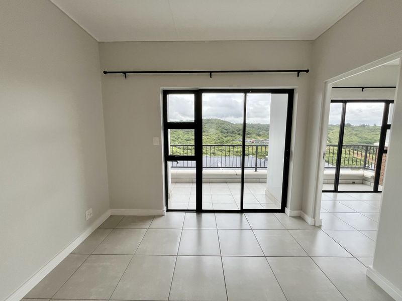 An empty, well-maintained living area featuring neutral tiled floors and large sliding glass doors that open onto a balcony with scenic views.