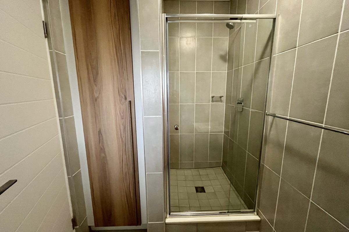 A clean, modern bathroom featuring a glass-enclosed shower, neutral wall tiling, and built-in wooden cabinetry for storage.