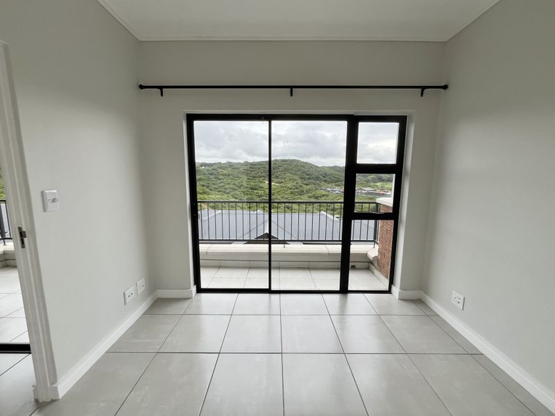 A bright, empty bedroom featuring neutral tiled flooring, modern sliding glass doors leading to a balcony, and a scenic hillside view.