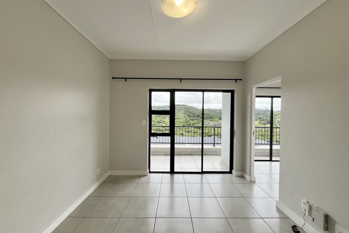 A bright, empty living area featuring neutral tiled flooring and large sliding glass doors that open onto a balcony with scenic views.
