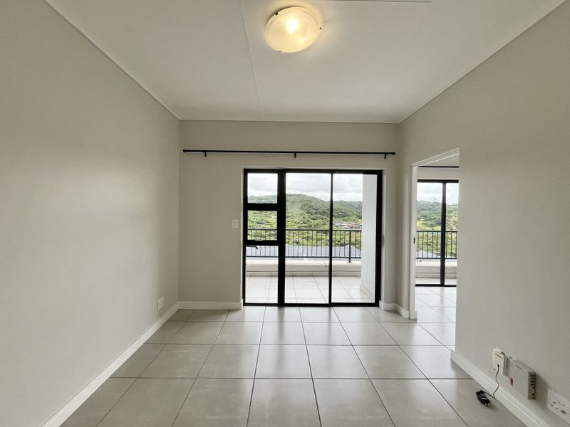 A bright, empty living area featuring neutral tiled flooring and large sliding glass doors that open onto a balcony with scenic views.