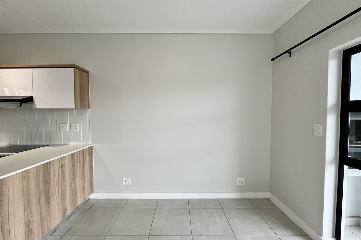 A clean, modern kitchen area featuring light wood-finish cabinetry, a sleek electric hob, tiled flooring, and neutral wall tones.