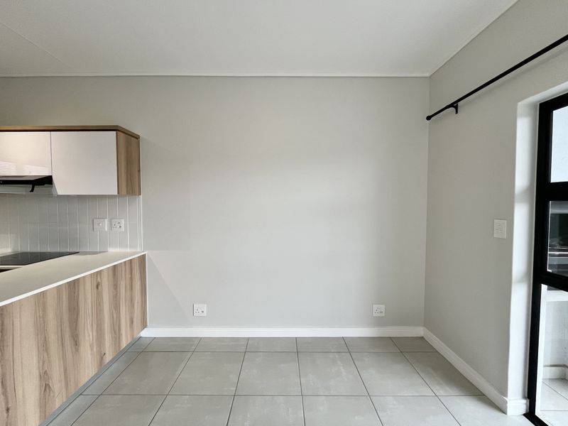 A clean, modern kitchen area featuring light wood-finish cabinetry, a sleek electric hob, tiled flooring, and neutral wall tones.