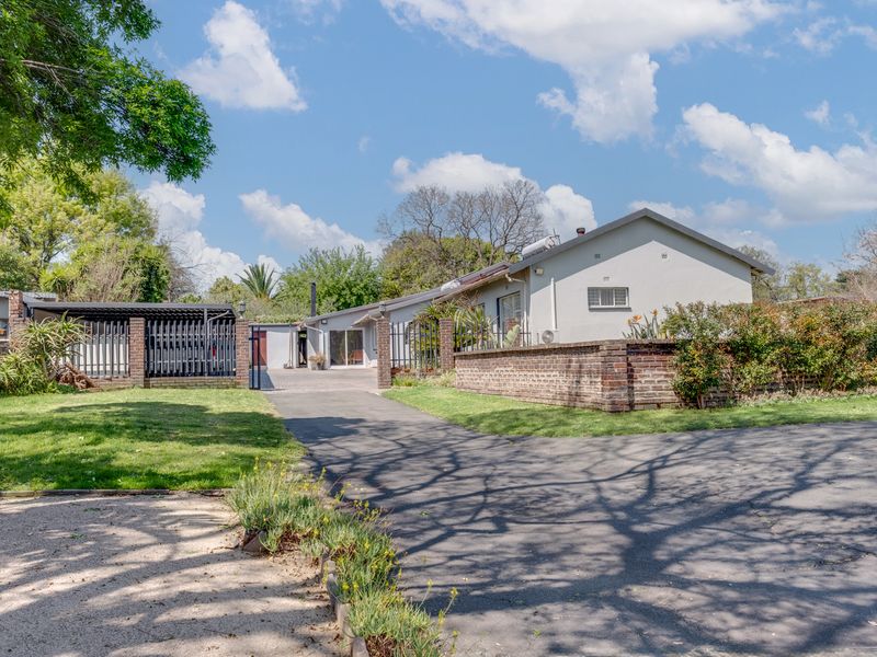 Front exterior view of the property featuring a paved driveway, brick boundary wall, and a carport, set within a landscaped garden area.