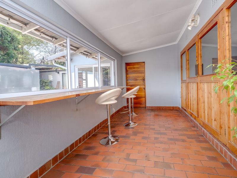 A covered patio area featuring terracotta tile flooring, a built-in wooden bar counter, and wooden framed glass doors leading into the home.