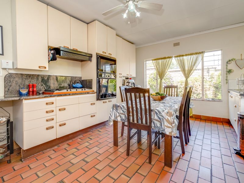 A functional kitchen featuring built-in cabinetry, granite countertops, integrated oven, and a dining area with terracotta tiled flooring.