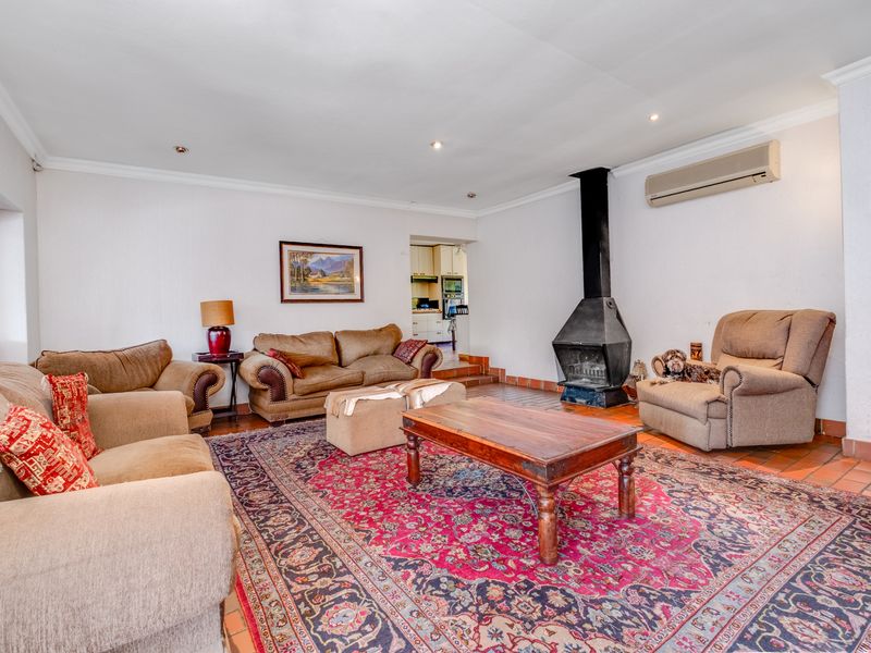 Spacious living room featuring terracotta tile flooring, a prominent freestanding fireplace, and a wall-mounted air conditioning unit, with an open transition to the kitchen area.