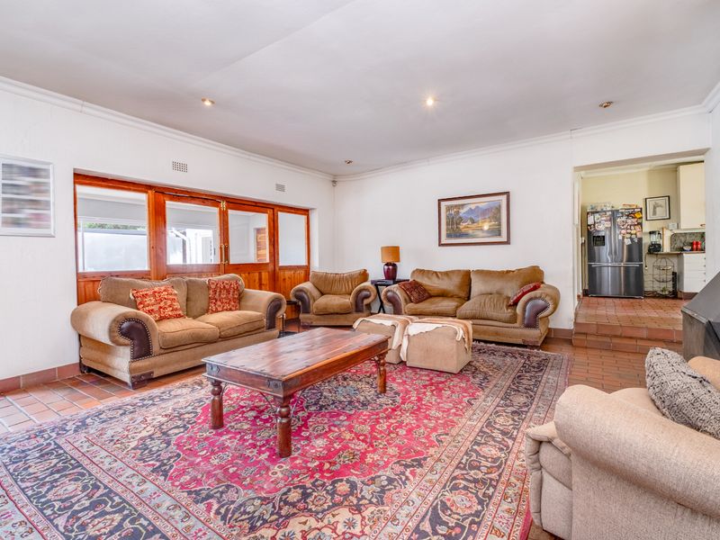 Spacious open-plan living area featuring terracotta tile flooring, a built-in fireplace, and wooden framed glass doors leading to the exterior.