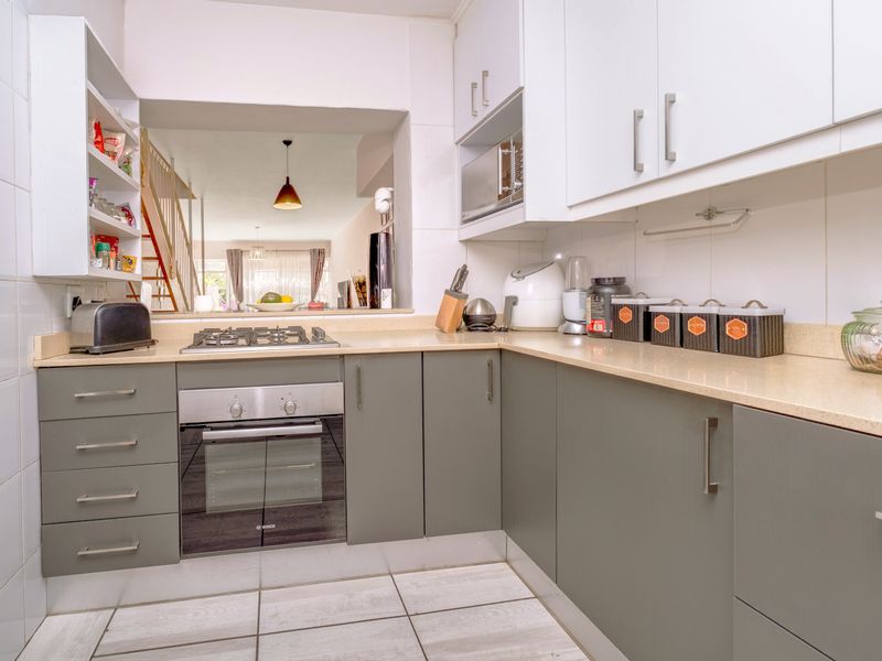 A functional kitchen featuring built-in cabinetry, stone countertops, a gas hob, and an integrated oven, with a convenient serving hatch to the living area.