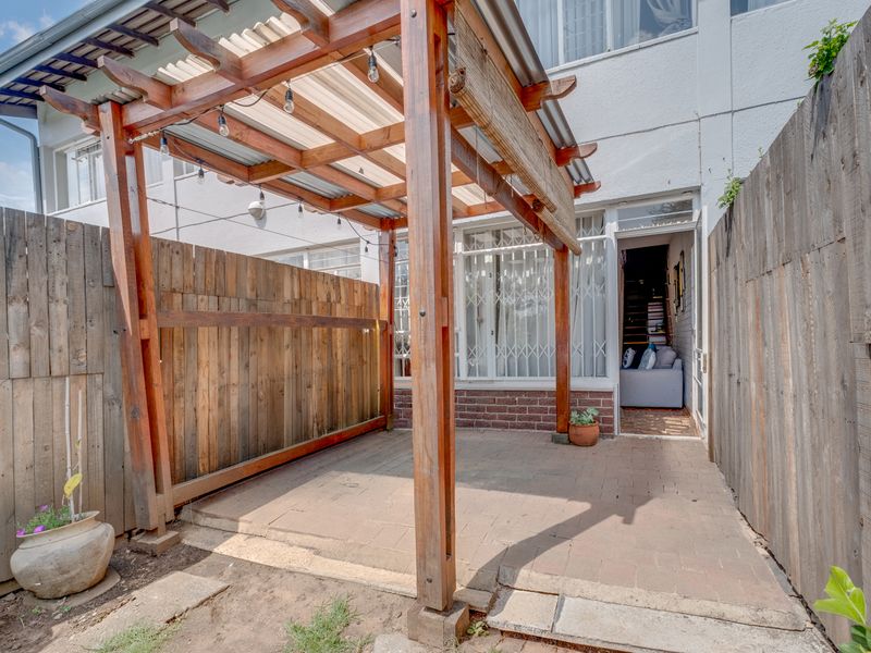 A private rear courtyard featuring a timber pergola over a paved patio area, enclosed by wooden fencing and providing access to the apartment interior.