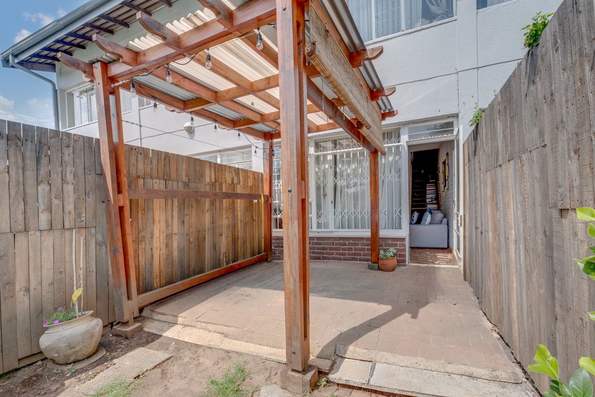 A private rear courtyard featuring a timber pergola over a paved patio area, enclosed by wooden fencing and providing access to the apartment interior.