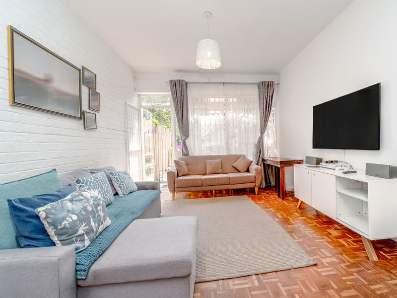 A bright living room featuring classic parquet flooring, a textured white brick feature wall, and direct access to an outdoor area through a glass door.