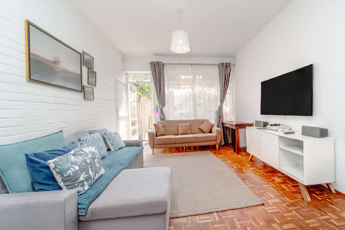 A bright living room featuring classic parquet flooring, a textured white brick feature wall, and direct access to an outdoor area through a glass door.