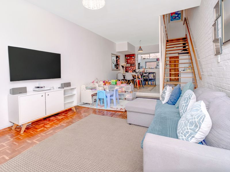 Open plan living area featuring parquet flooring, an exposed brick feature wall, and a staircase leading to the upper level.