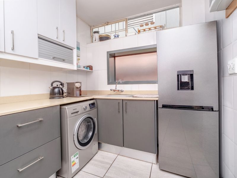A functional laundry area featuring built-in grey cabinetry, a stainless steel sink, laminate countertops, and tiled finishes.