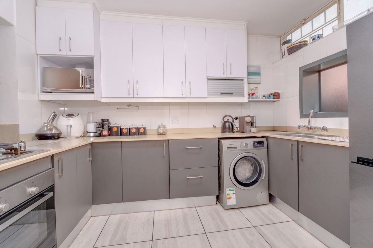 A functional kitchen featuring modern grey and white cabinetry, laminate countertops, built-in oven, hob, and an integrated washing machine with tiled flooring.