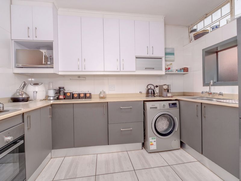 A functional kitchen featuring modern grey and white cabinetry, laminate countertops, built-in oven, hob, and an integrated washing machine with tiled flooring.