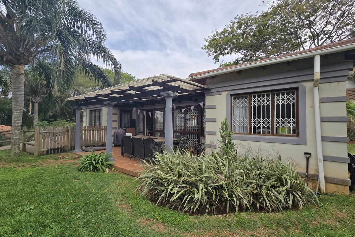 Rear view of the house featuring a covered patio with a pergola, established garden, and security bars on the windows.