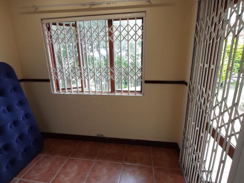 A vacant bedroom featuring tiled flooring, ceiling fan, and security gates on both the window and sliding door.