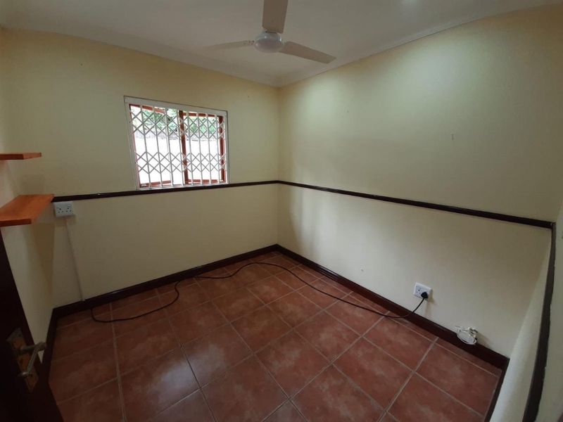 An empty bedroom featuring tiled flooring, a ceiling fan, and security bars on the window, providing a blank canvas for potential updates.