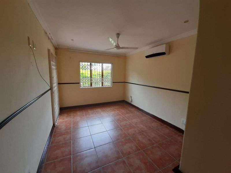 An empty bedroom featuring tiled flooring, a ceiling fan, a wall-mounted air conditioner, and security bars on the window.