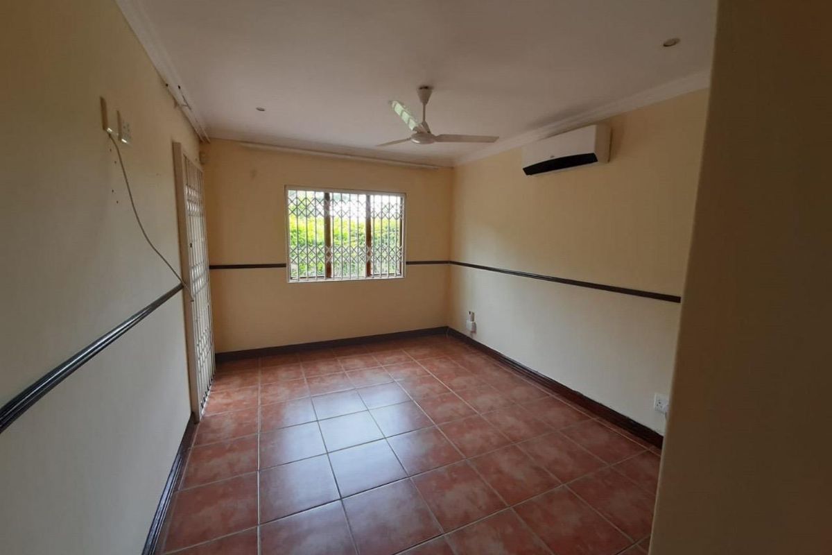 An empty bedroom featuring tiled flooring, a ceiling fan, a wall-mounted air conditioner, and security bars on the window.