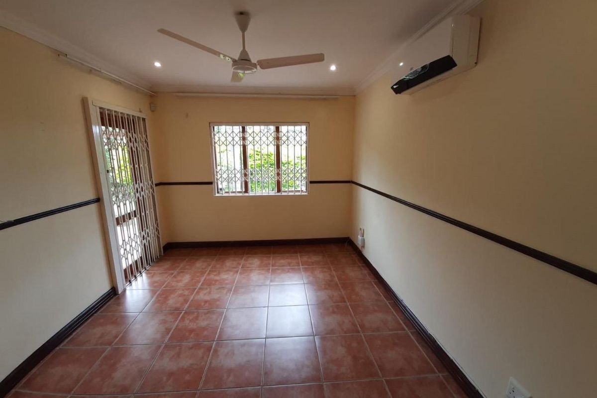 An empty living room featuring tiled flooring, a ceiling fan, a wall-mounted air conditioner, and security fixtures on the door and window.