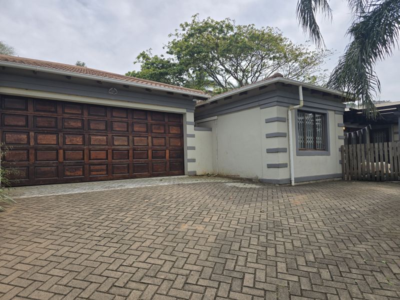Front exterior view of the property featuring a paved driveway, a large wooden garage door, and a tiled roof structure.