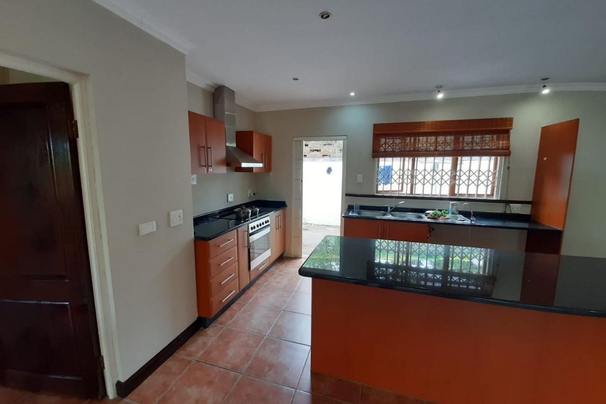 A functional kitchen featuring wooden cabinetry, granite countertops, a built-in oven with extractor fan, and tiled flooring with direct access to the exterior.