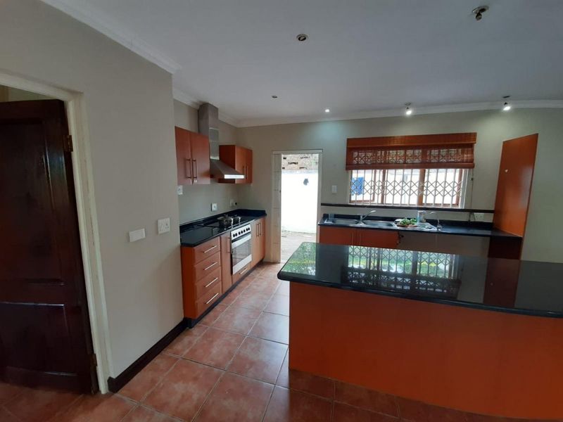 A functional kitchen featuring wooden cabinetry, granite countertops, a built-in oven with extractor fan, and tiled flooring with direct access to the exterior.