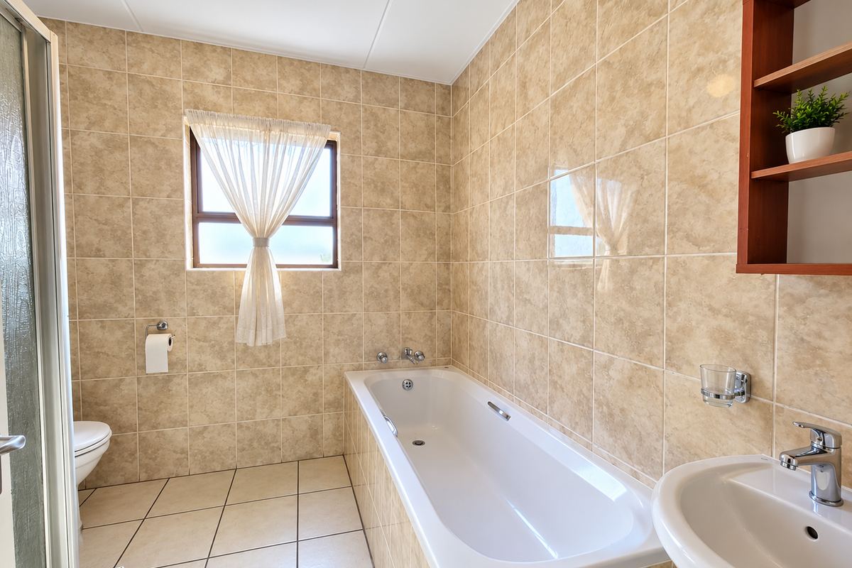 A functional bathroom featuring a built-in bathtub, wall-mounted basin, shower enclosure, and neutral ceramic tiling throughout.