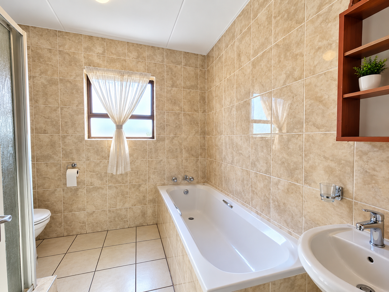 A functional bathroom featuring a built-in bathtub, wall-mounted basin, shower enclosure, and neutral ceramic tiling throughout.