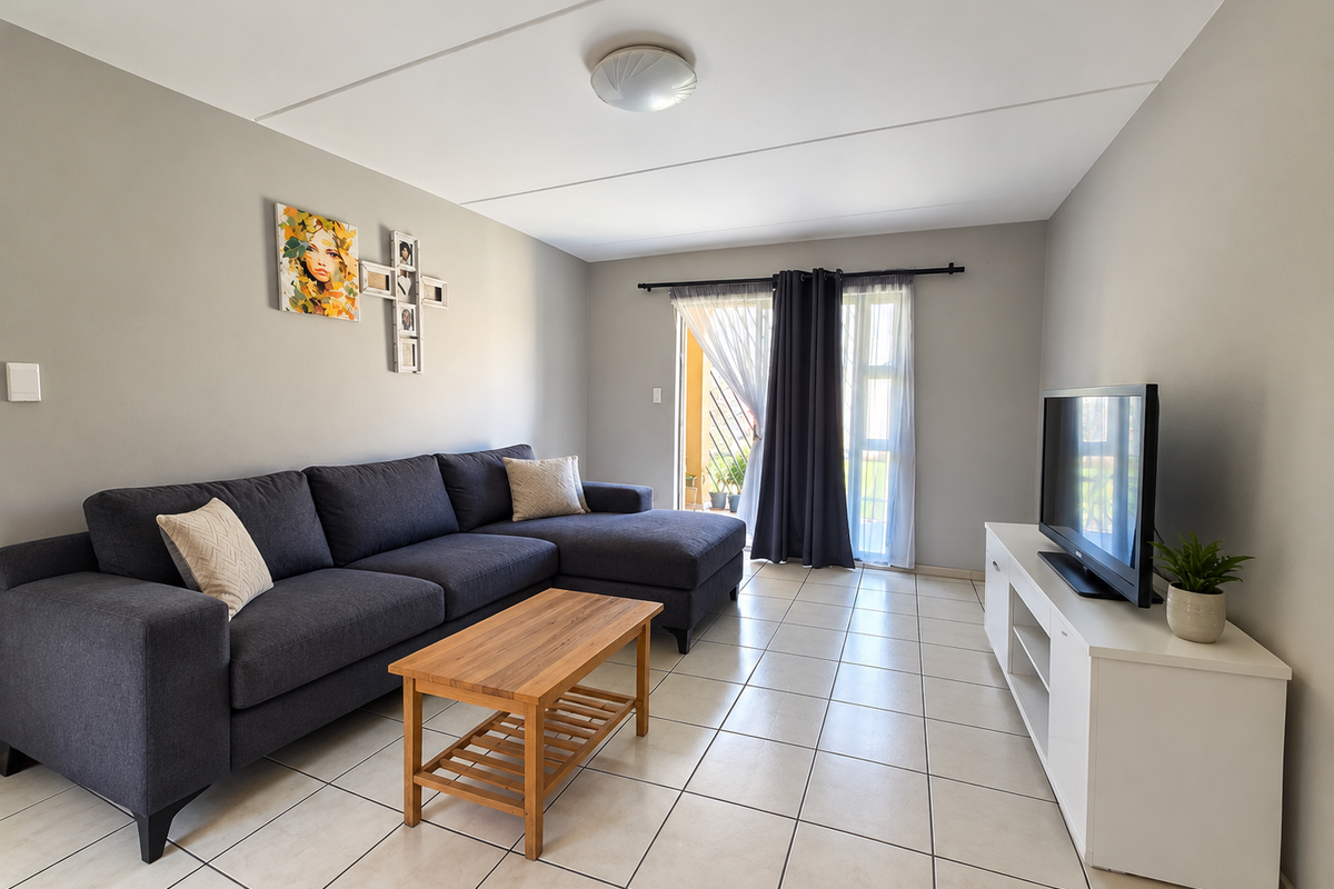A well-maintained living room featuring neutral tiled flooring, light grey walls, and a sliding glass door providing access to an outdoor area.