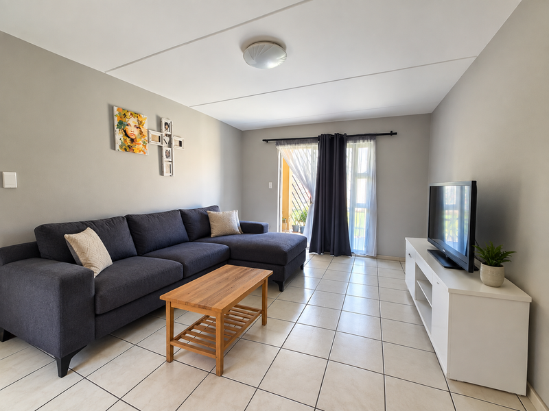 A well-maintained living room featuring neutral tiled flooring, light grey walls, and a sliding glass door providing access to an outdoor area.