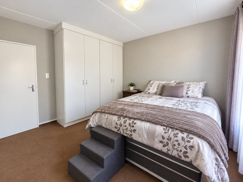 A well-maintained bedroom featuring neutral wall tones, fitted floor-to-ceiling built-in cupboards, and carpeted flooring, providing a clean and functional living space.