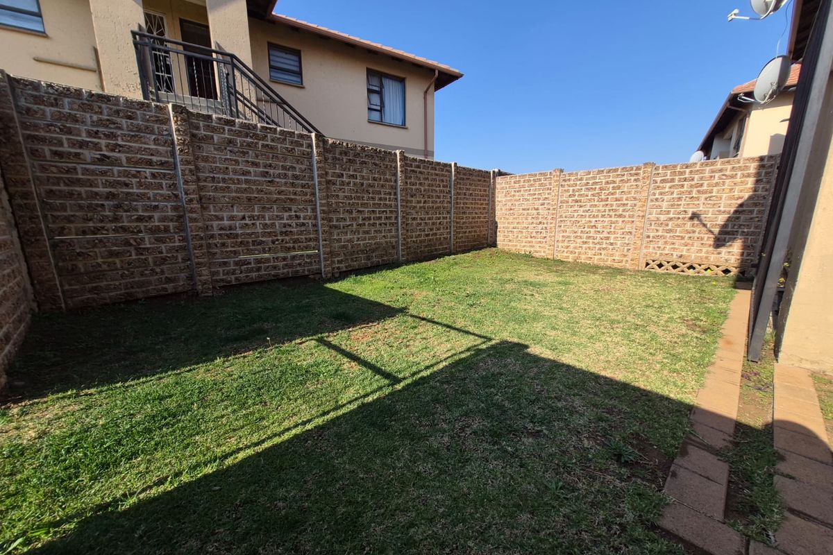 A private rear garden area featuring a well-maintained lawn, paved walkway, and secure brick boundary walls.