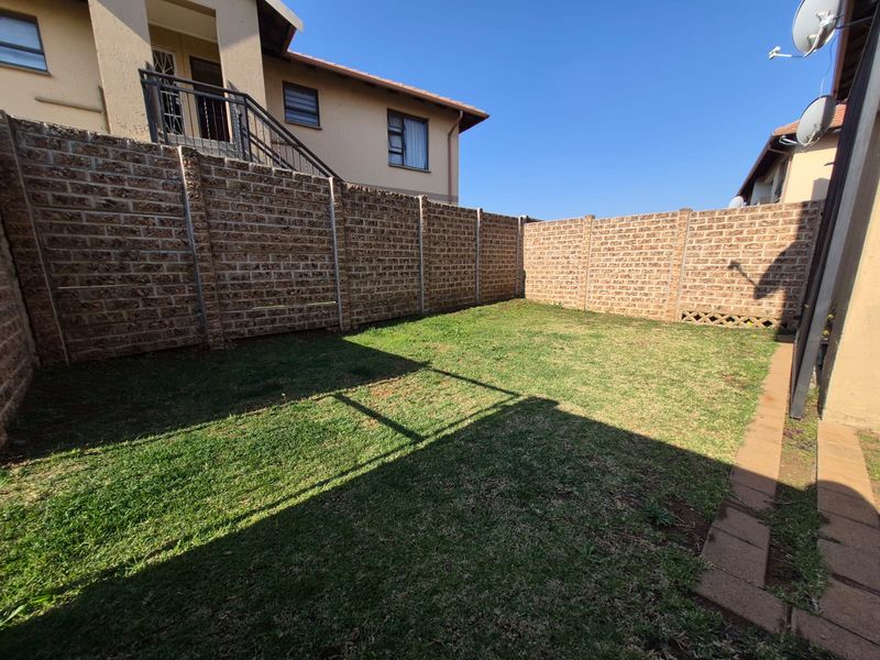 A private rear garden area featuring a well-maintained lawn, paved walkway, and secure brick boundary walls.