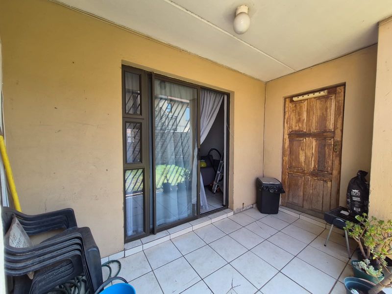 A covered patio area featuring tiled flooring, a sliding glass door entrance, and a weathered wooden door leading into the apartment.