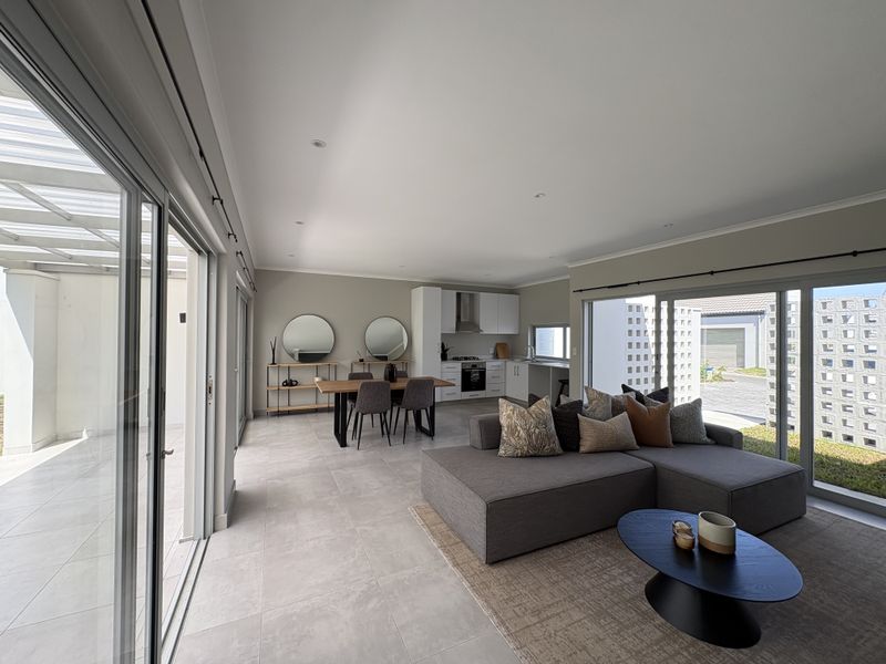 Spacious open-plan living and dining area featuring a modern kitchen with built-in appliances, tiled floors, and large sliding doors leading to an outdoor patio.