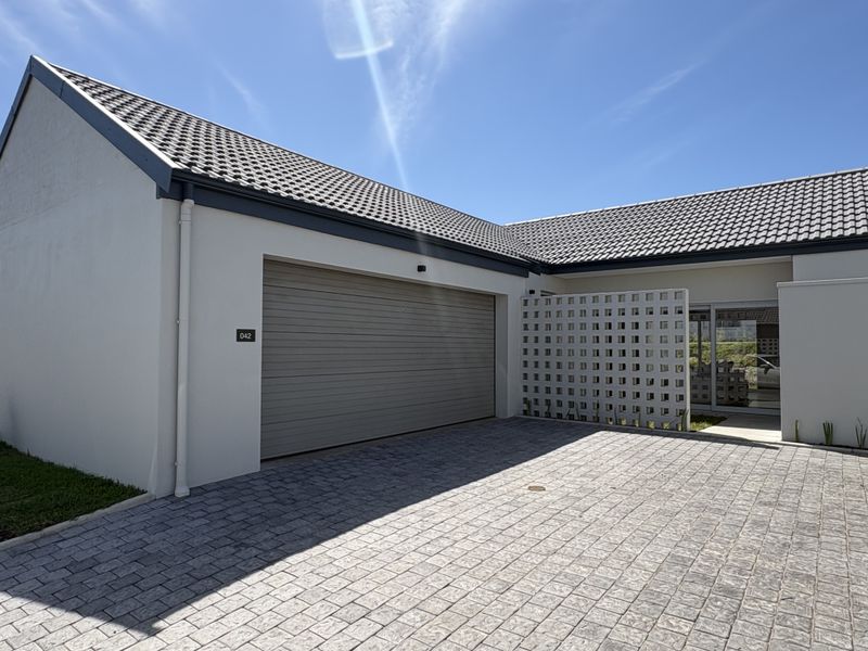 Front elevation of the property featuring a paved driveway, a single garage door, and a decorative concrete breeze block privacy screen.