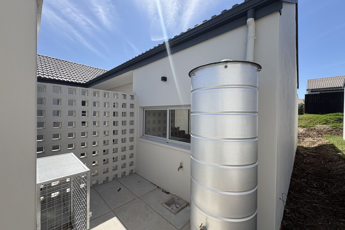 Rear exterior area featuring a metal water tank, tiled patio surface, decorative breeze block privacy screen, and functional drainage and water access points.