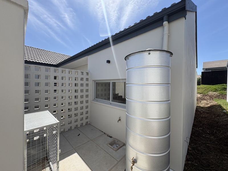 Rear exterior area featuring a metal water tank, tiled patio surface, decorative breeze block privacy screen, and functional drainage and water access points.