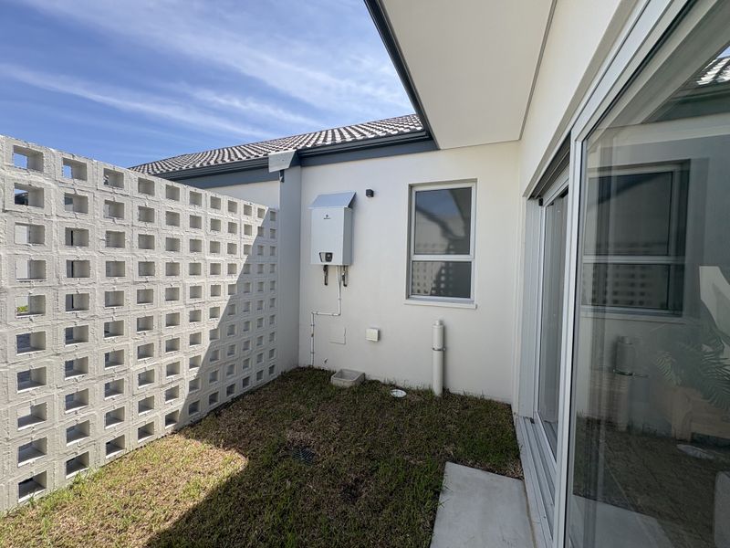 A private rear courtyard area featuring a breeze block boundary wall, a wall-mounted gas geyser, and access via a large sliding glass door.