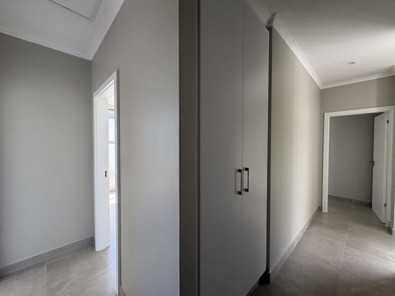 A clean, modern hallway featuring neutral wall tones, tiled flooring, and built-in storage cupboards with contemporary hardware.
