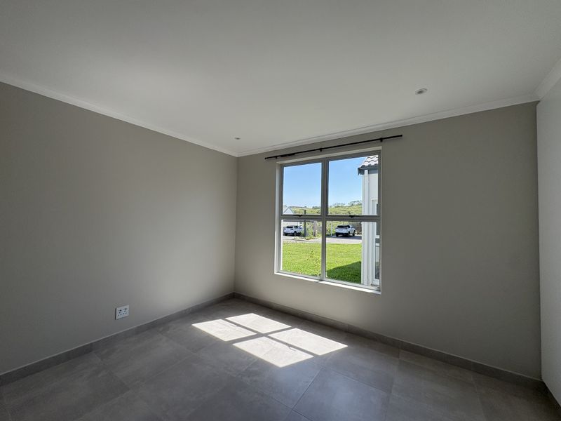 A bright, empty bedroom featuring neutral wall tones, large aluminium-framed windows, and modern tiled flooring.