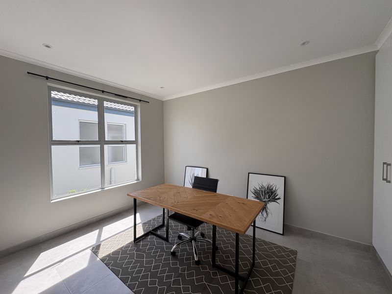 A bright and modern home office featuring neutral wall tones, tiled flooring, recessed lighting, and a built-in cupboard for storage.
