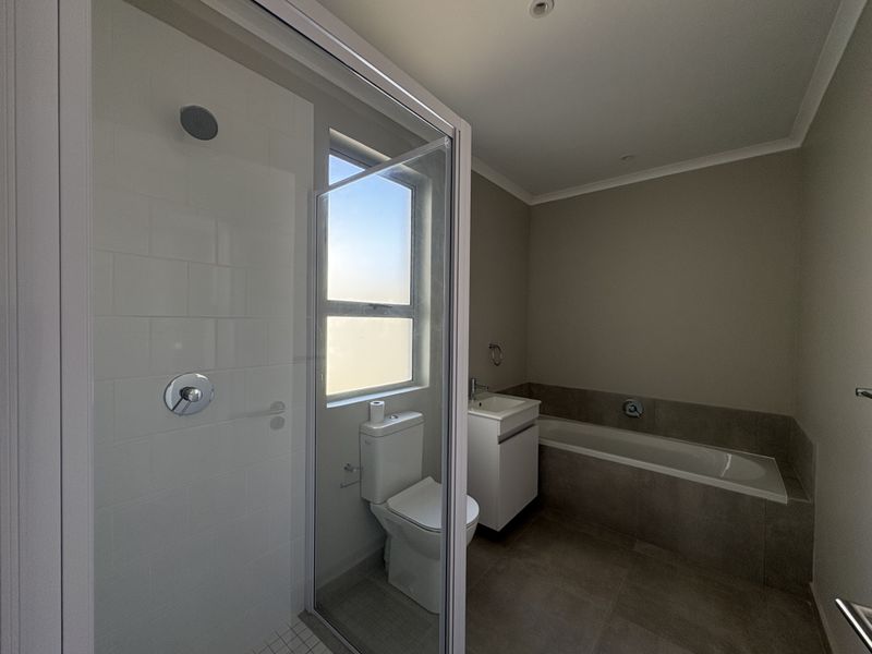 A modern, clean bathroom featuring a glass-enclosed shower, a built-in bathtub, a vanity basin, and a toilet with neutral floor and wall tiling.