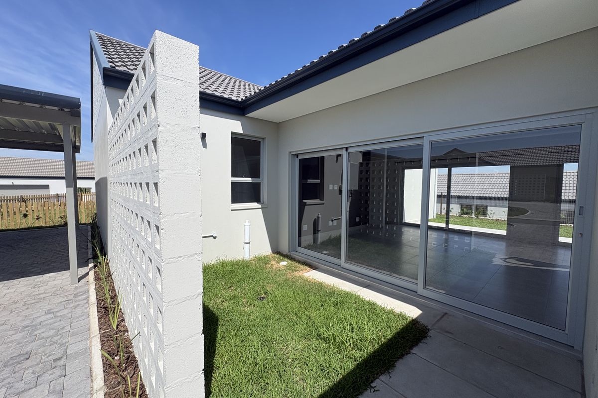 A modern rear exterior view featuring a paved patio, sliding glass doors, and a decorative breeze block wall with a small lawn area.