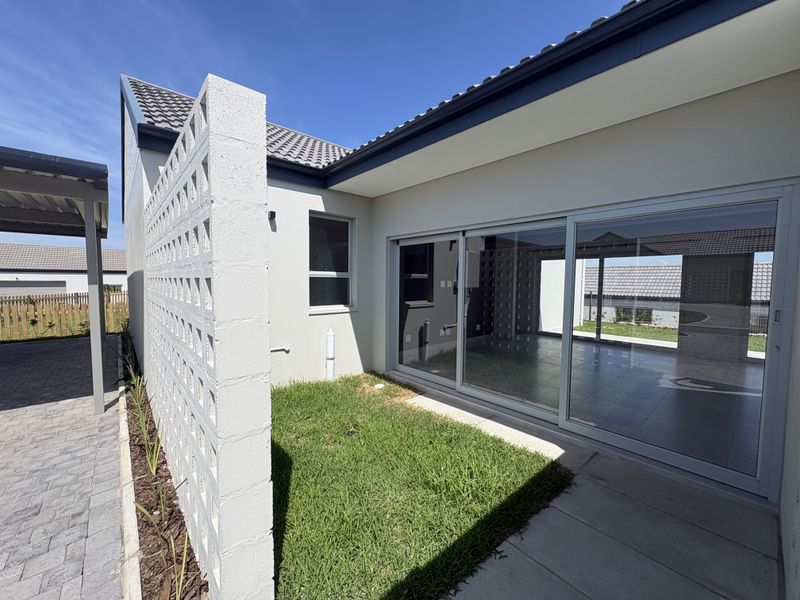 A modern rear exterior view featuring a paved patio, sliding glass doors, and a decorative breeze block wall with a small lawn area.